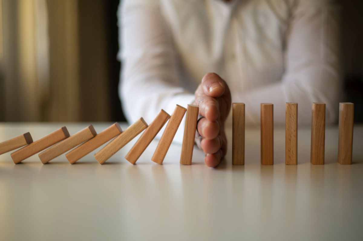 hand stops dominoes knocking over others illustrating intervention to manage risk